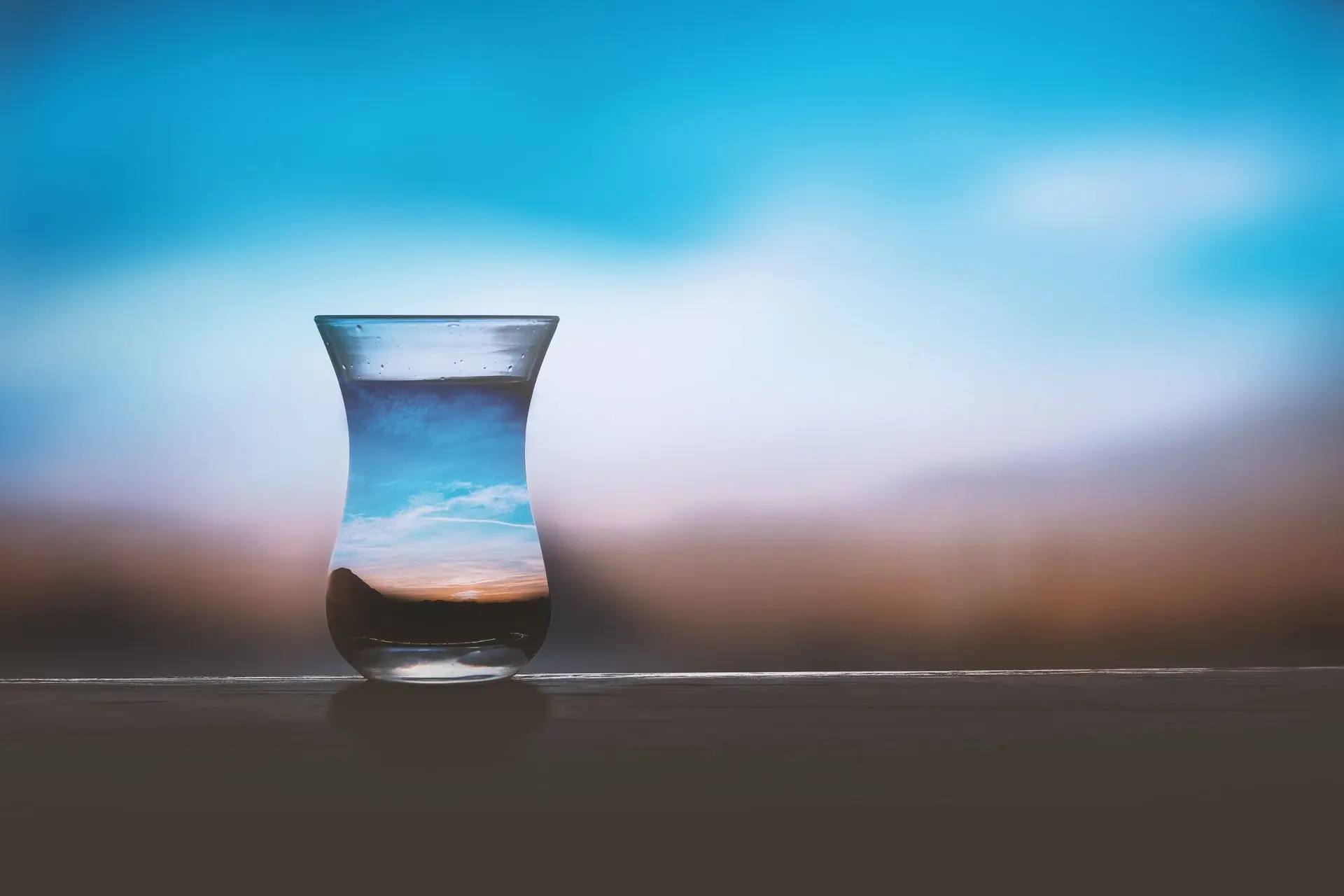 Verre d’eau transparent sur une surface, reflet du ciel bleu et du coucher de soleil, évoquant le thème « boisson pendant un jeûne hydrique ».