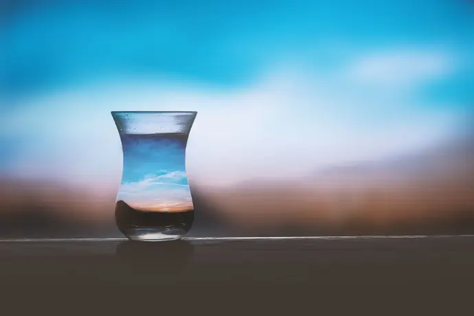 Verre d'eau sur une surface sombre avec un ciel bleu flou en arrière-plan, symbolisant le jeûne. comment bien faire un jeûne d'une semaine